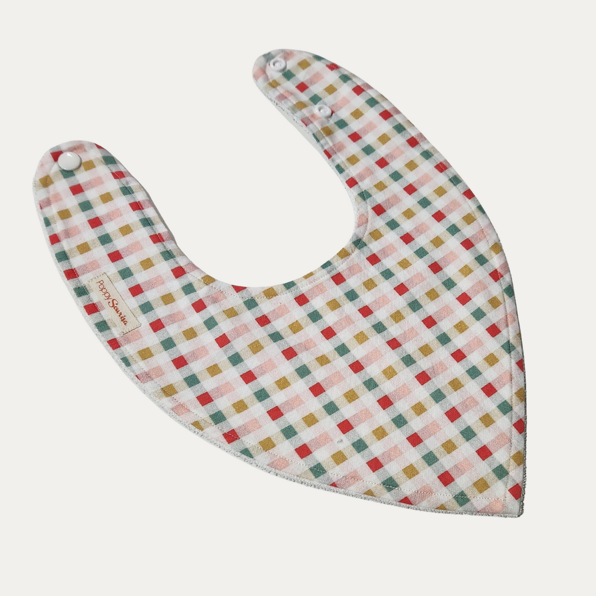 Christmas Tartan baby dribble bib featuring red, green, mustard and pale pink checks on a cream background.