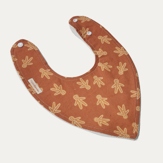 Gingerbread Man Christmas baby dribble bib featuring outlined gingerbread figures on a warm rust background.