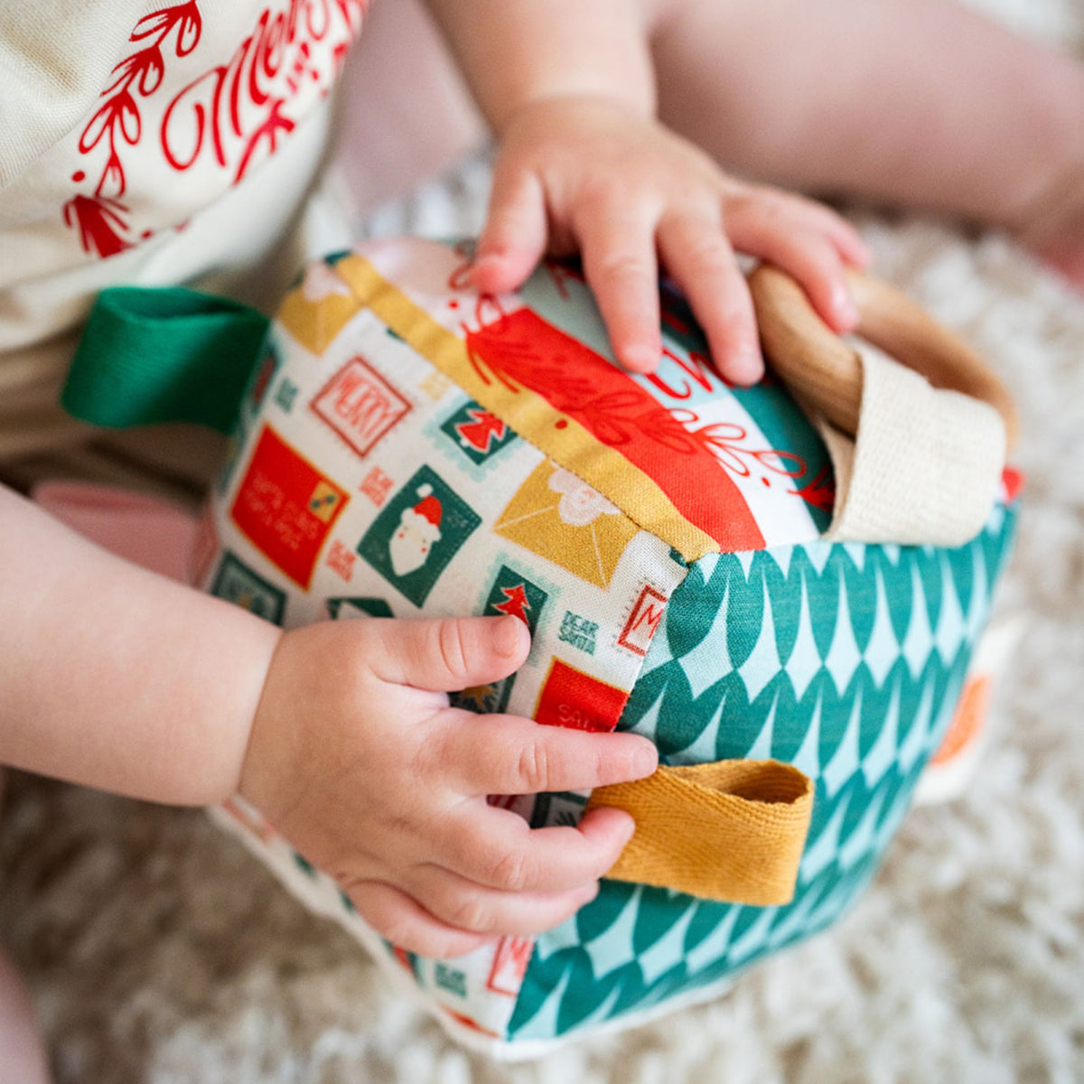 Baby’s hands exploring the ribbon tags and wooden ring on a handmade Christmas sensory cube with a Santa stamp print