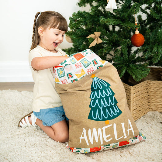 A delighted little girl opening her personalised gold Santa Sack named Amelia, with a Christmas tree design