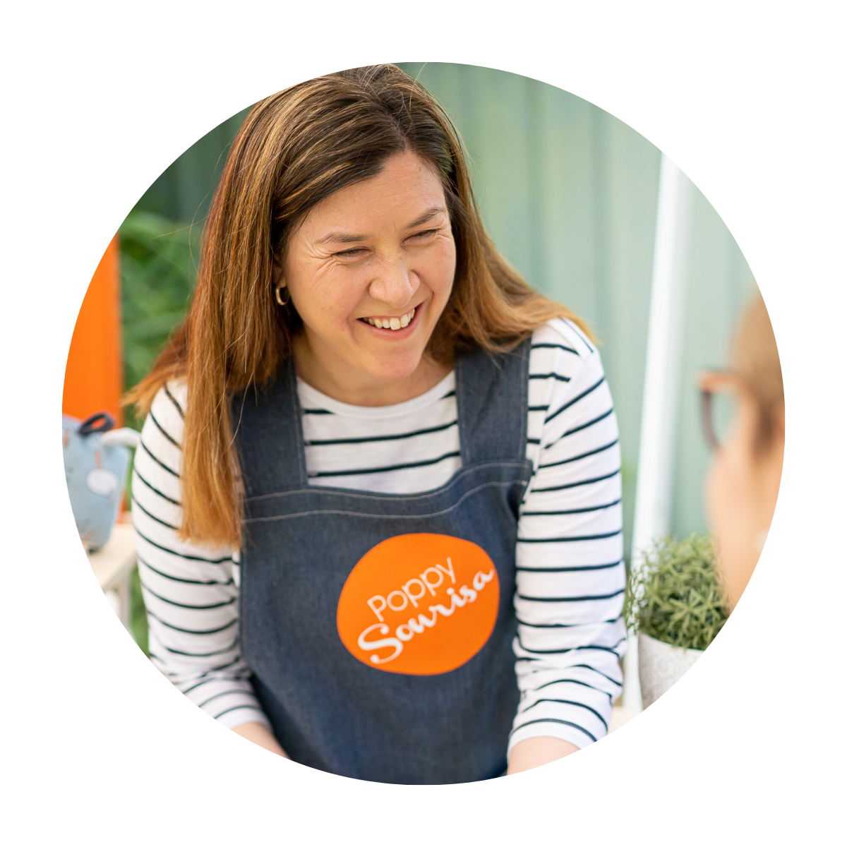 Maker Mia, founder of Poppy Sonrisa, smiling in her denim apron with the orange Poppy Sonrisa logo