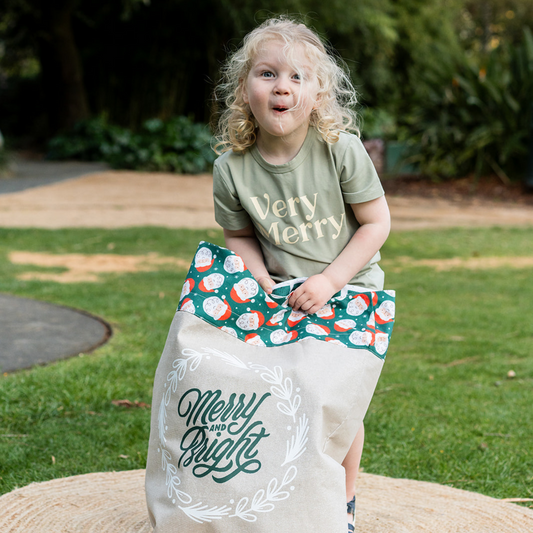 Child holding a linen Santa Sack with a Merry Santa printed top and ‘Merry and Bright’ design on the front