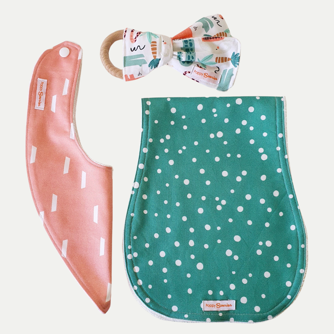 Handmade newborn gift pack with a coral dribble bib, sage green spotted burp cloth and safari print bow rattle on a wooden ring