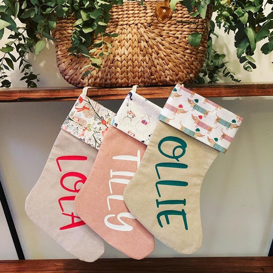 Three personalised Christmas stockings hanging together, with printed festive cuffs and the names Lola, Tilly and Ollie