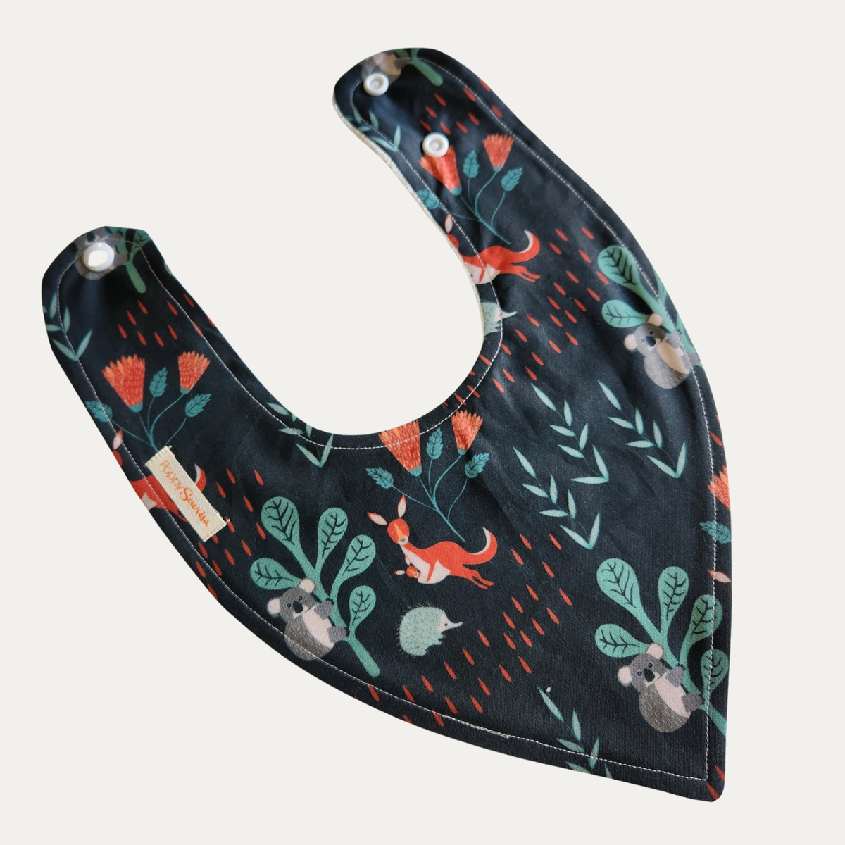 Aussie Animals baby dribble bib featuring kangaroos, koalas and native foliage on a dark background, with adjustable snap fasteners.