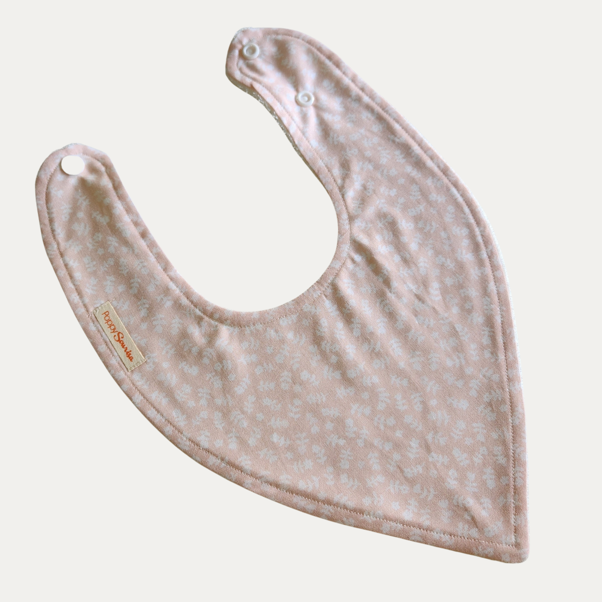 Ballerina baby dribble bib in soft pink with small white spots and adjustable white snap fasteners.