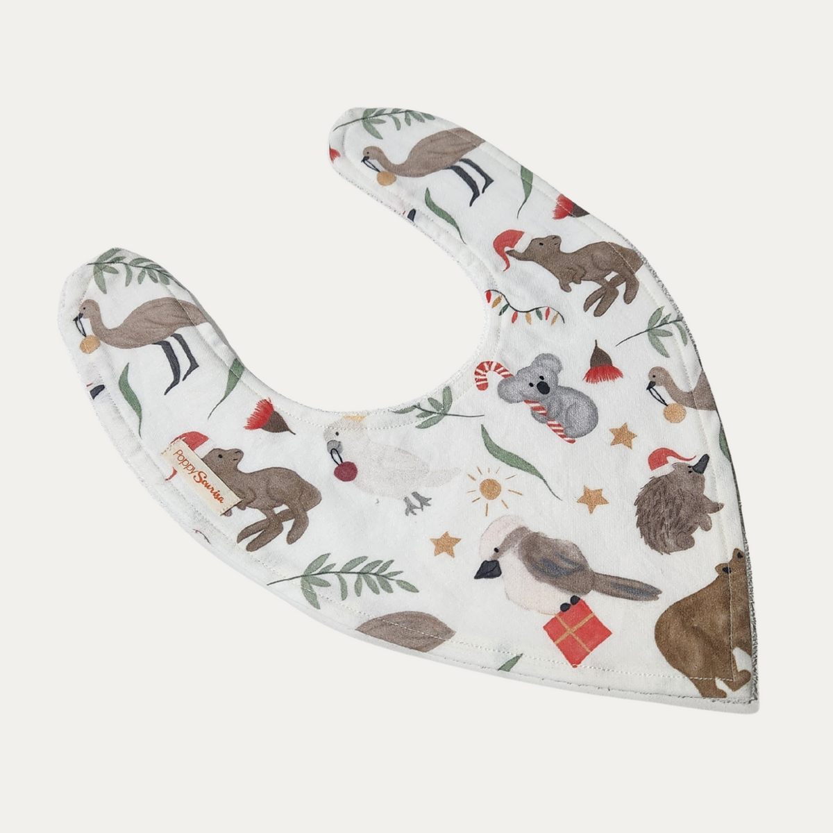 Christmas Down Under baby dribble bib featuring Australian animals, Santa hats, gifts and native foliage on a cream background.