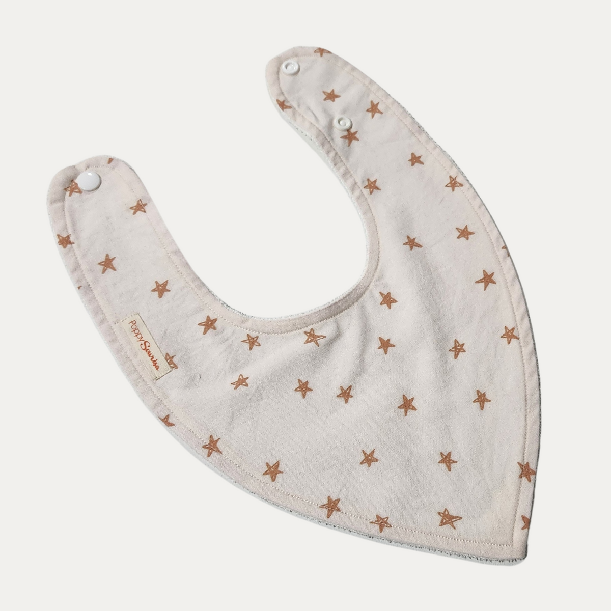 Christmas Stars baby dribble bib featuring small hand-drawn rust-coloured stars on a cream background, with adjustable white snaps.