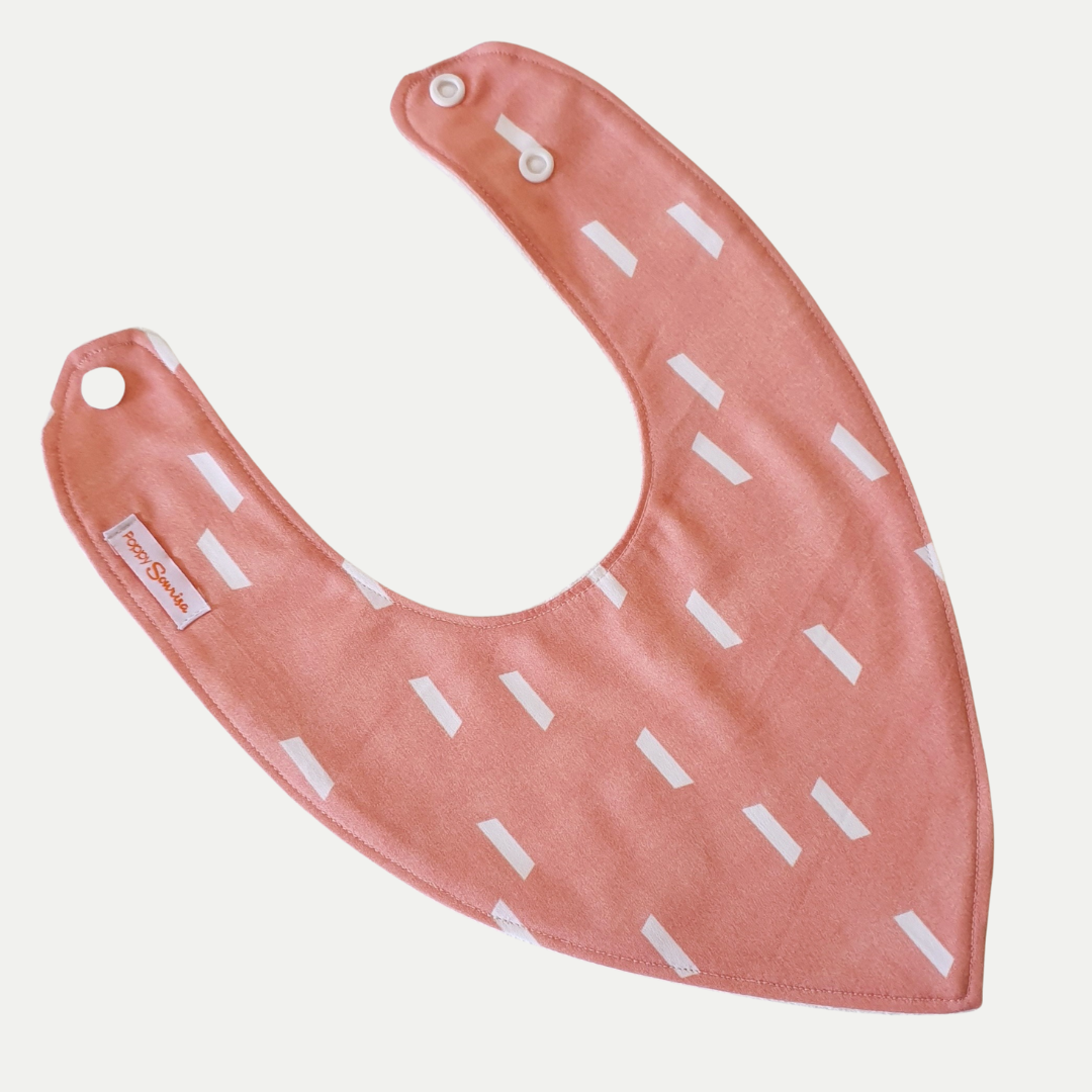 Baby dribble bib with short white diagonal strokes on a soft coral background.