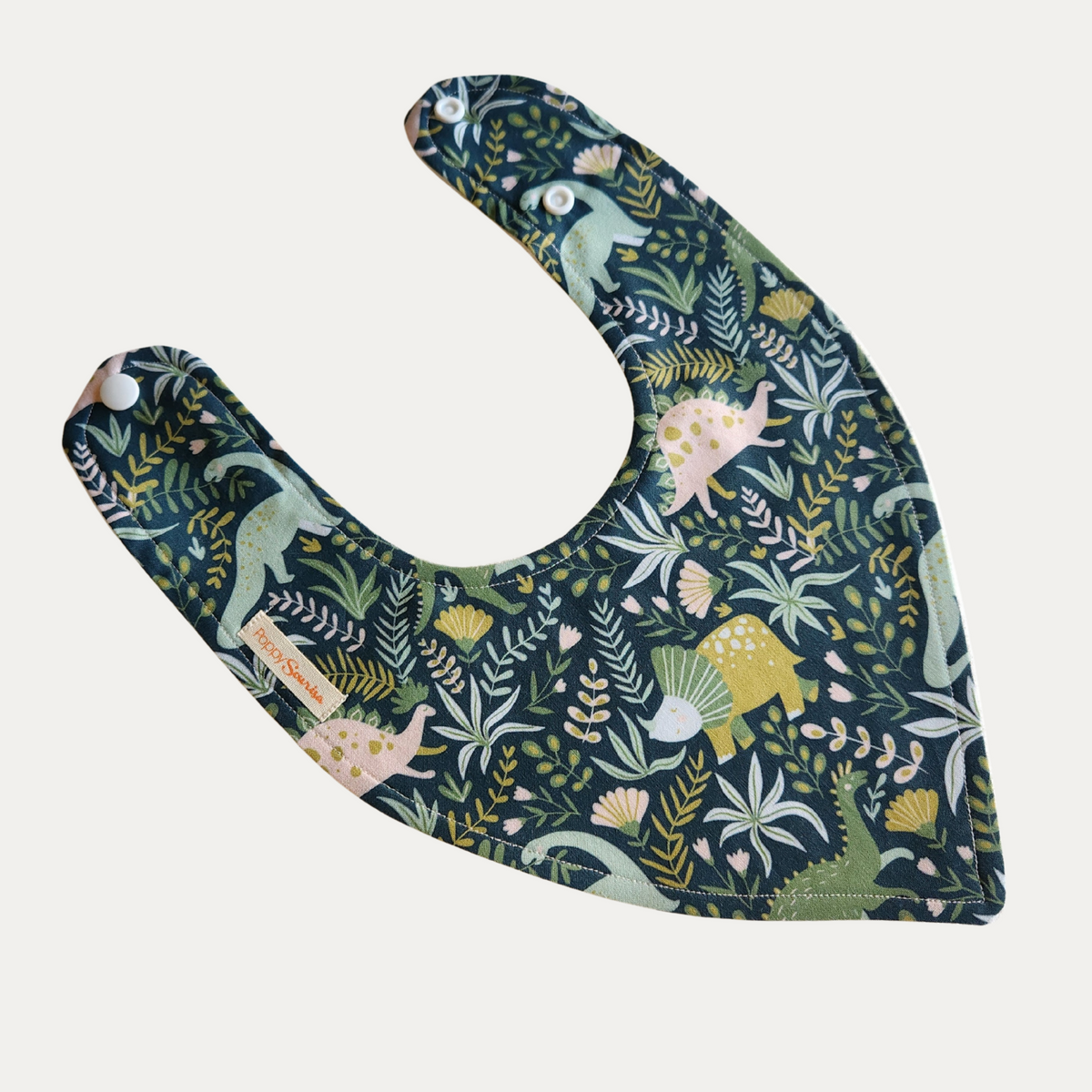 Baby dribble bib with pastel dinosaurs amongst green leaves and small flowers on a dark teal background.