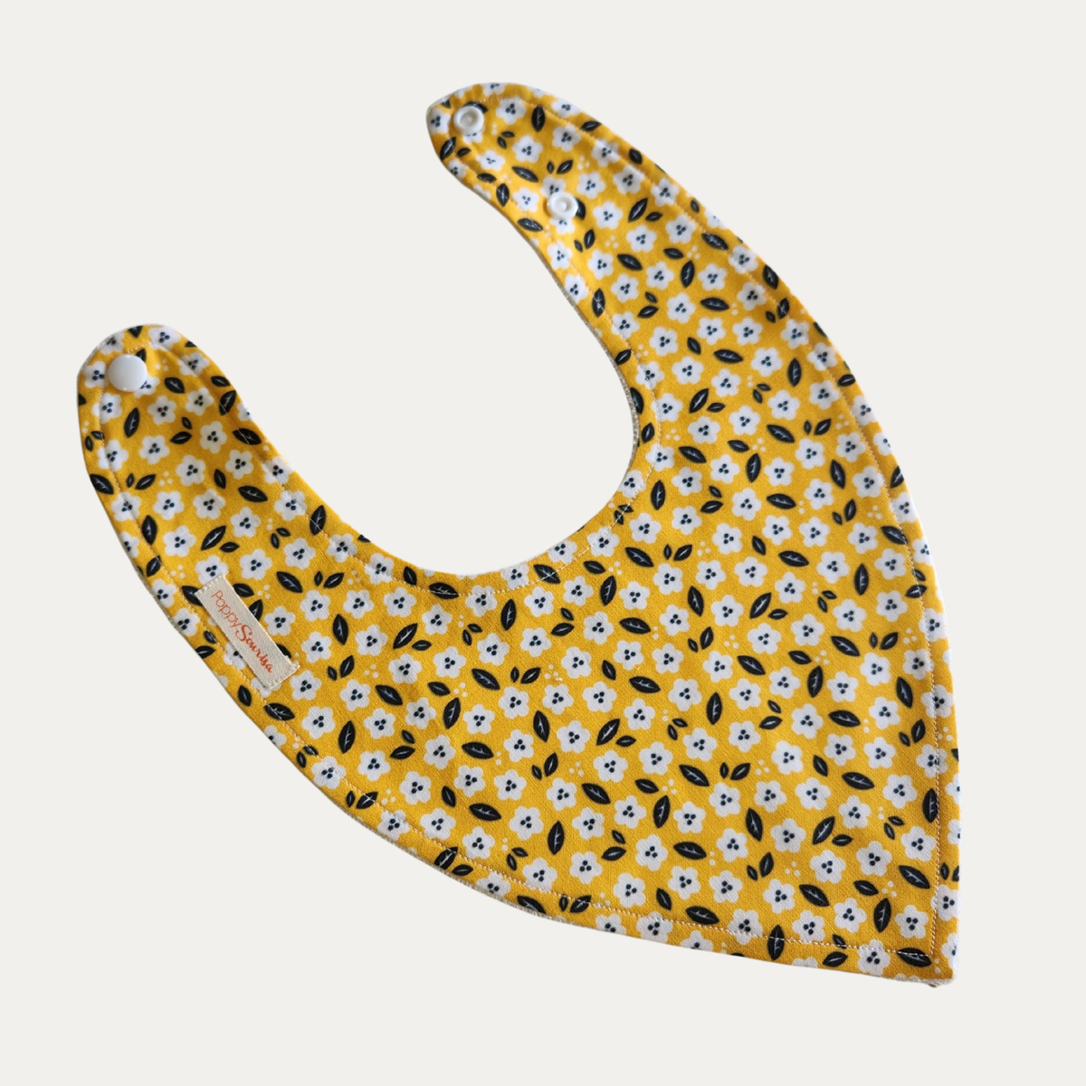Ditsy baby dribble bib featuring small white flowers and dark leaves on a mustard yellow background, with adjustable white snaps.