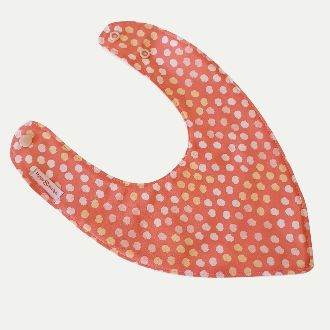 Baby dribble bib with textured pale pink and yellow dots on a coral background.
