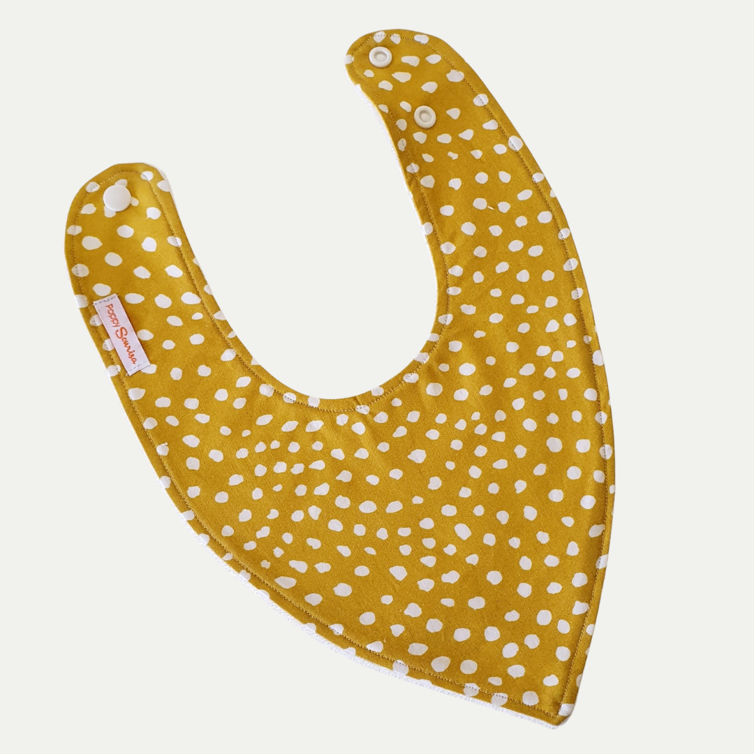 Baby dribble bib with small irregular cream spots on a marigold yellow background.