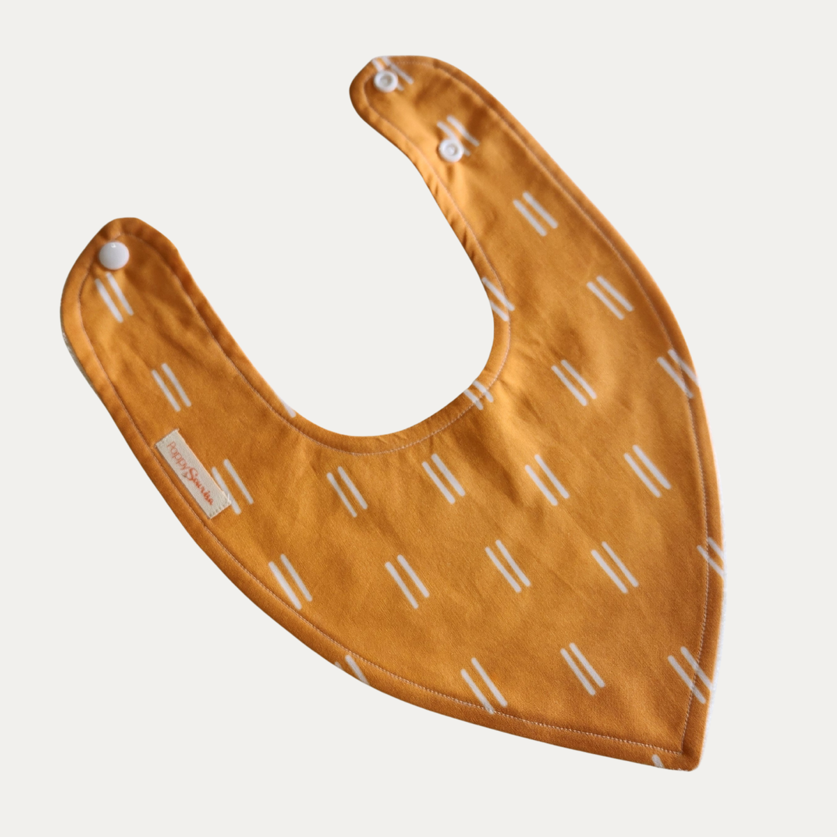 Mustard Mudcloth baby dribble bib featuring pairs of short white lines on a mustard background, with adjustable white snaps.