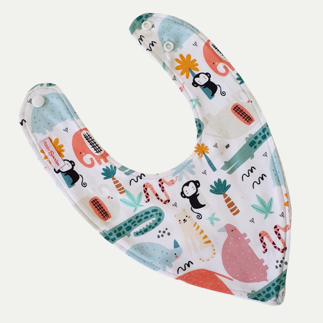 On Safari baby dribble bib featuring colourful safari animals and tropical plants on a cream background, with adjustable snap fasteners.