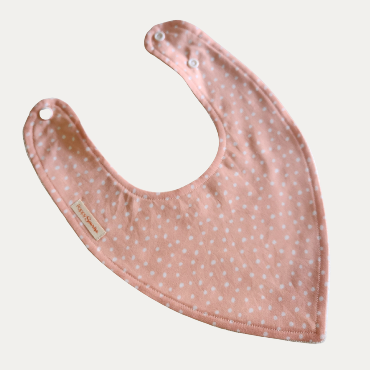 Baby dribble bib with tiny white spots on a soft peach background.