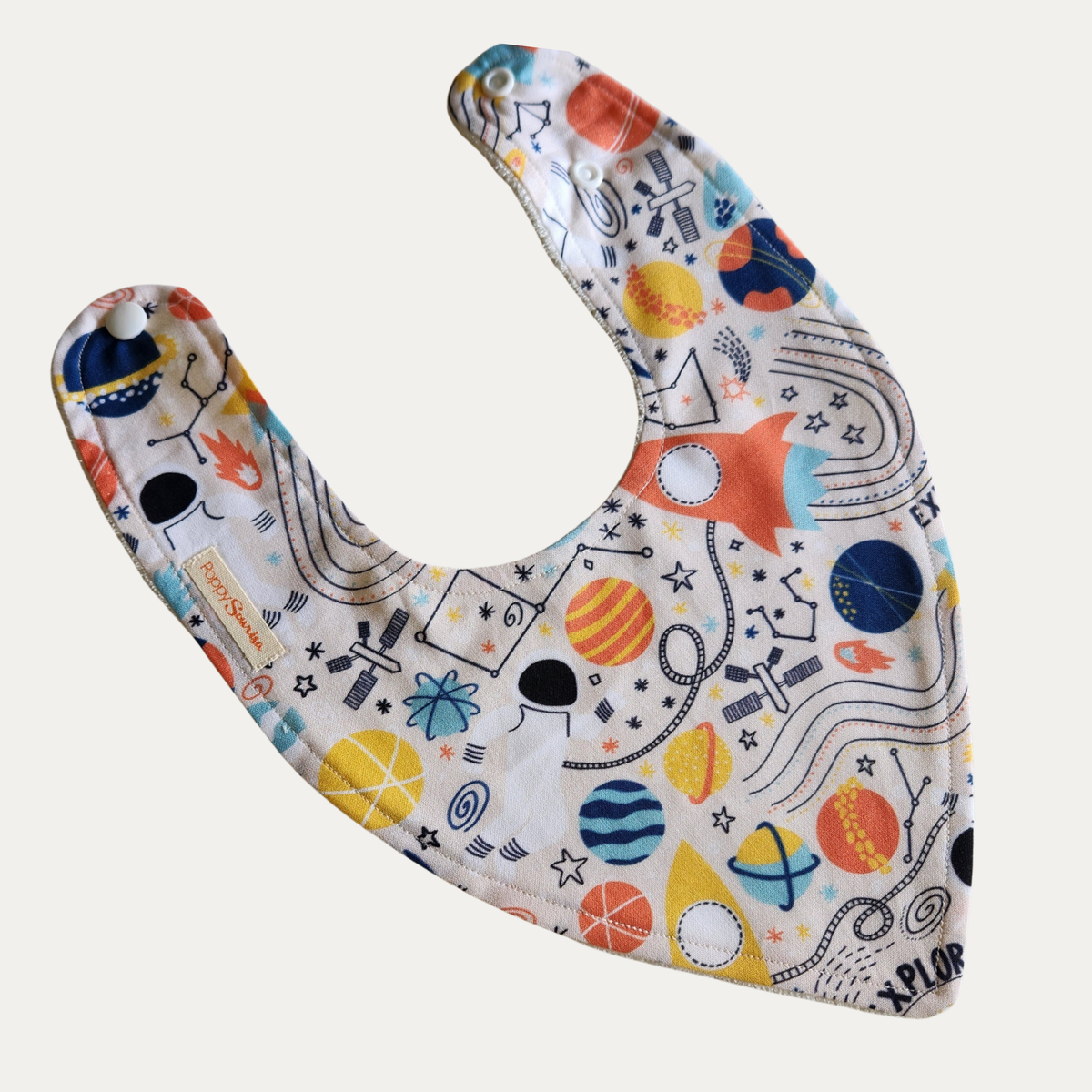 Baby dribble bib with colourful planets, rockets, stars and astronauts on a cream background.