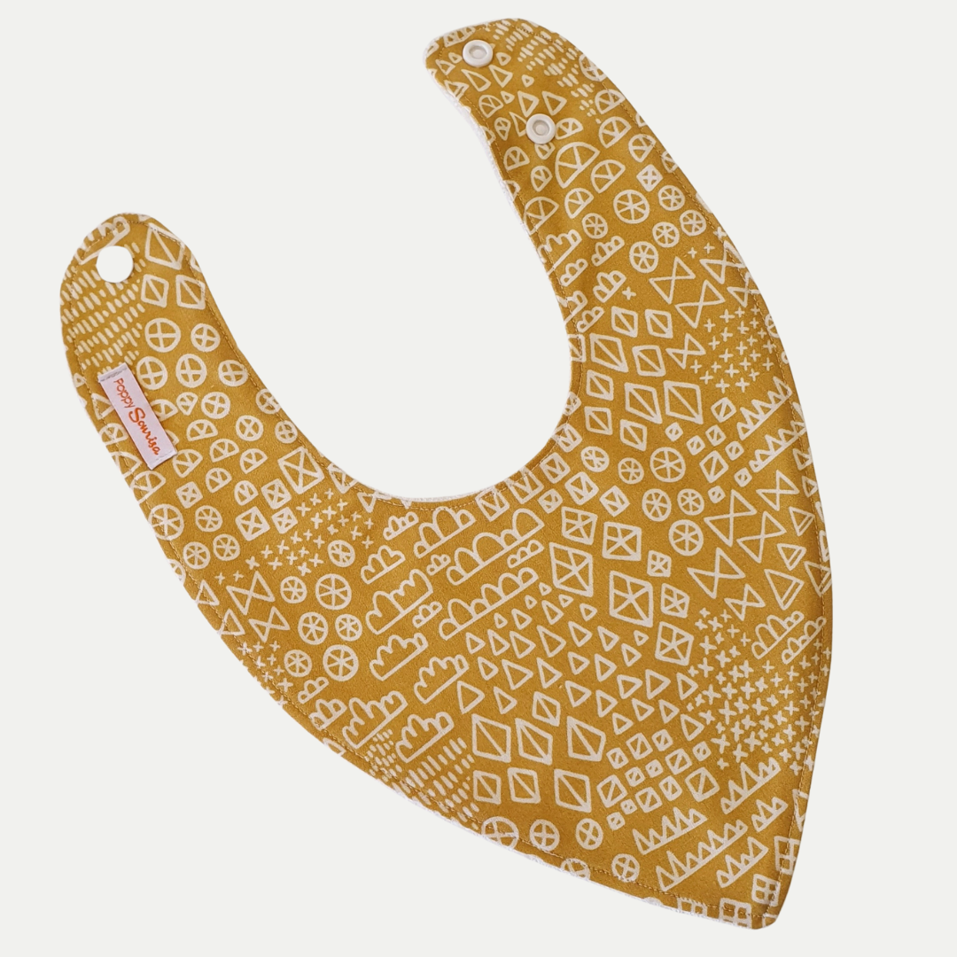 Baby dribble bib with cream hand-drawn circles, triangles, diamonds and crosses on a mustard background.