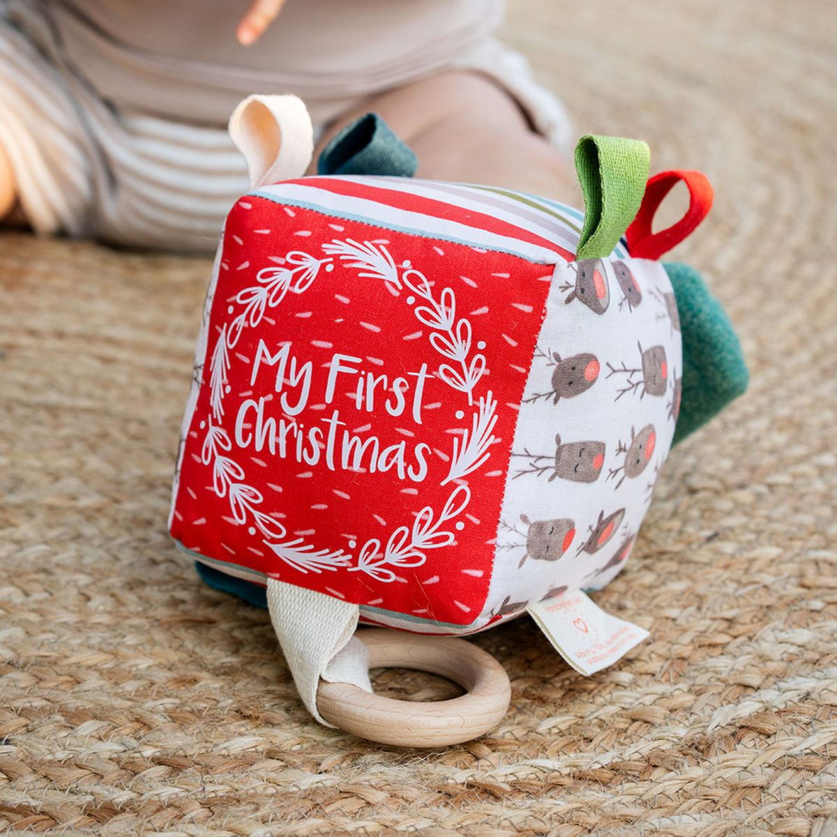 Baby lying down holding the Reindeer Herd My First Christmas sensory cube with wooden teething ring