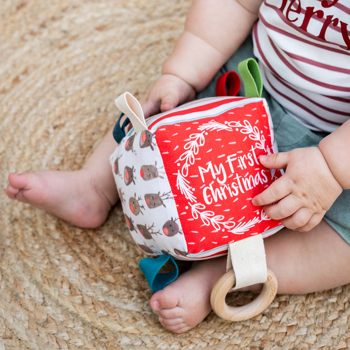 Baby sitting on a jute rug holding the Reindeer Herd My First Christmas sensory cube