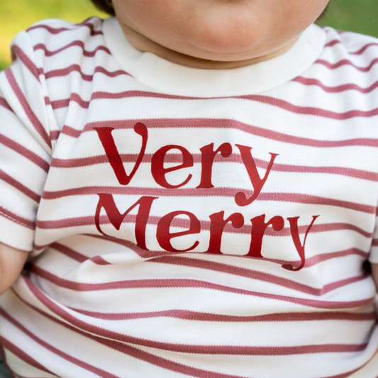 Close-up of a baby wearing a white and dusty pink striped tee with ‘Very Merry’ printed in red on the front